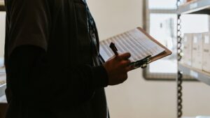 Pessoa confere um checklist em prancheta entre prateleiras de estoque
