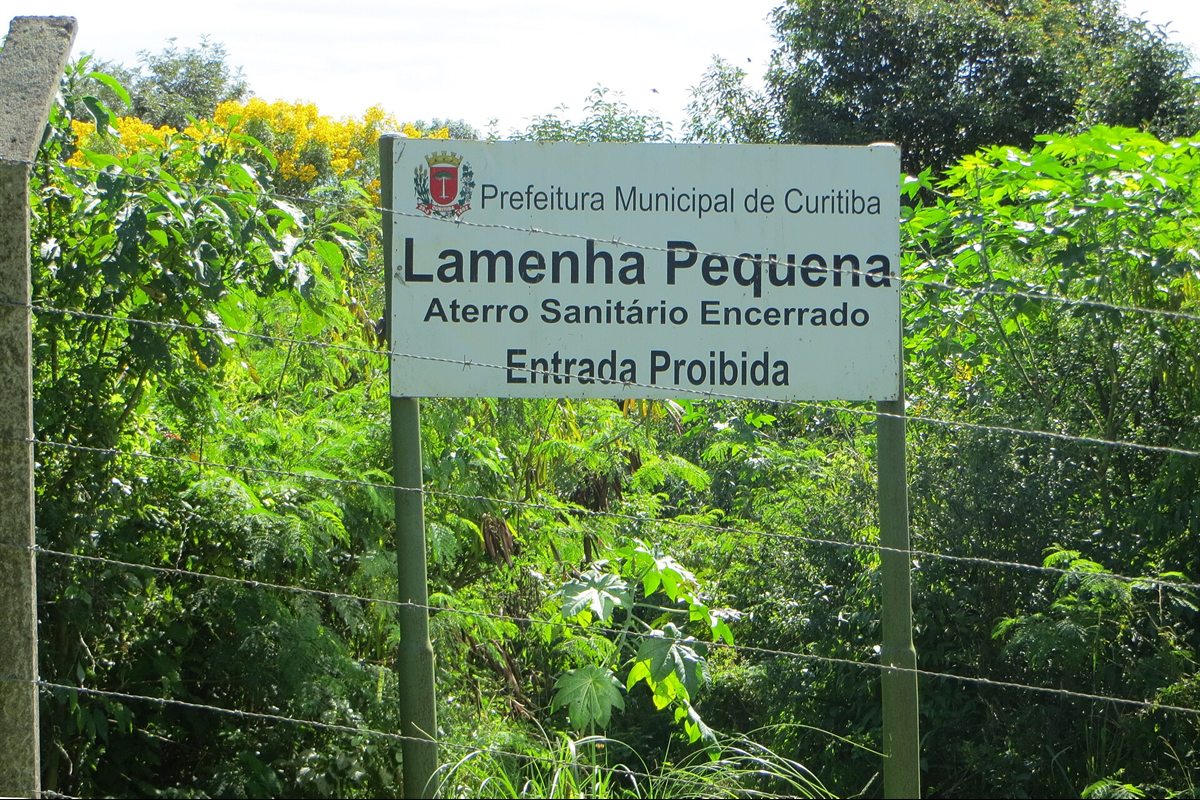 Placa de área de aterro encerrado com entrada proibida, cercada e com vegetação recuperada.