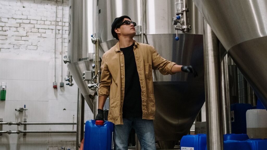 Operador carrega galão de produto químico entre tanques de aço inox em uma pequena indústria